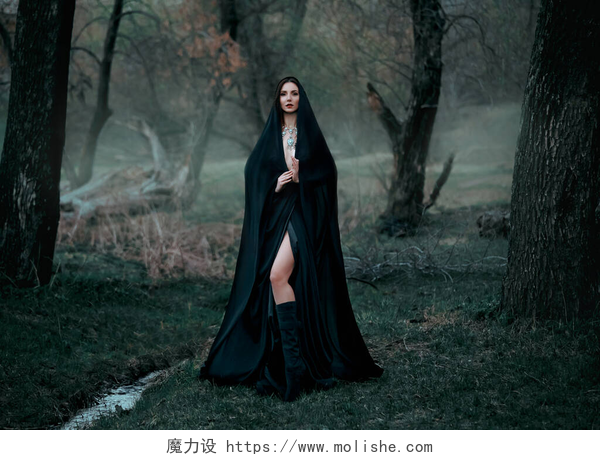 在森林里穿着黑色外套的女人神秘的幻想哥特式女人被邪恶缠住了。穿着黑衣斗篷的女恶魔吸血鬼。走在密密麻麻的森林深处，树木丛生。中古女王穿著丝绸斗篷，围巾摆姿势